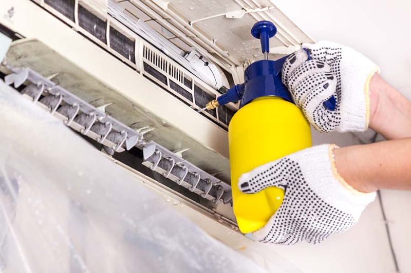 Blog Title- AC Maintenance Checklist Photo-Technician spraying chemical water onto air conditioner coil to clean and disinfect