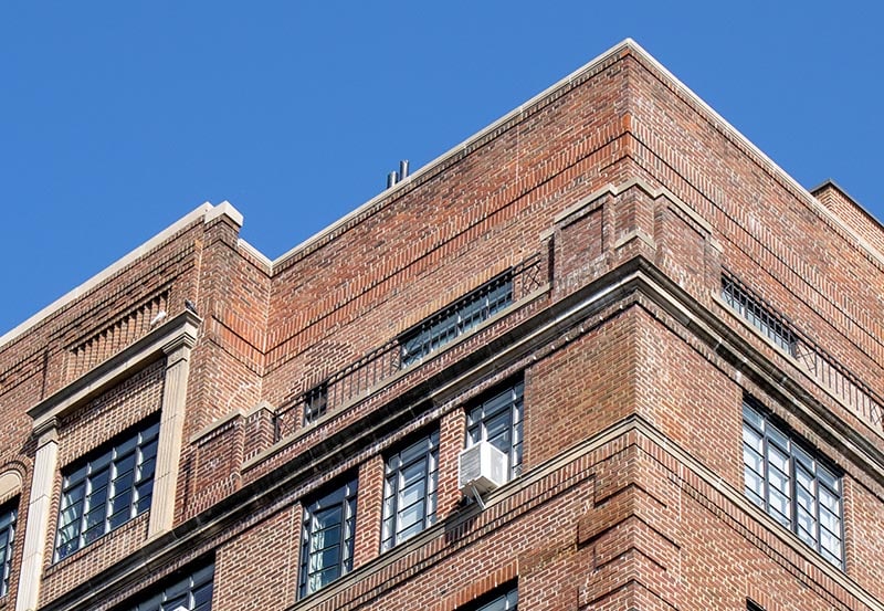 A low-angle view of the upper floors of a multi-story, classic brick building under a clear blue sky.