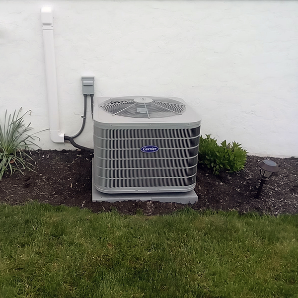 Carrier Air Conditioner Installation in Hollidaysburg, PA 16648 to the side of a white house with shrubbery planted next to it.
