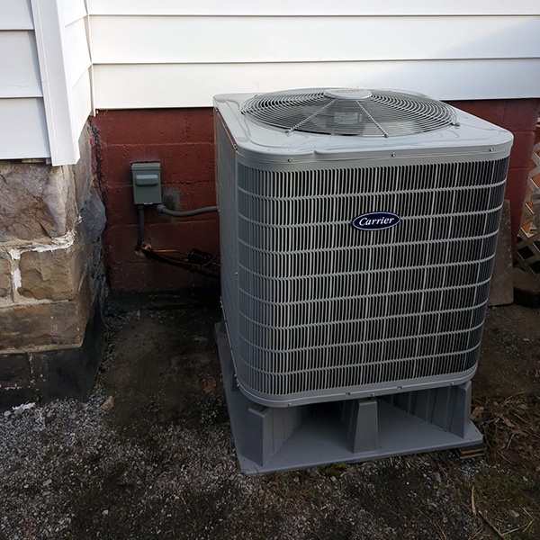 Carrier Heat Pump Installation in Revloc, PA 15948 outside of a red brick house with white siding.