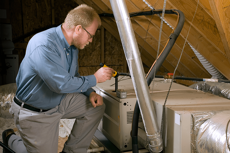 man fixing a furnace unit in an attic.