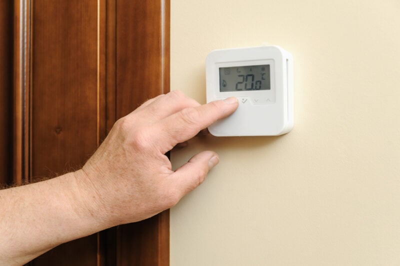Man is changing settings of a thermostat. His finger is pressing a button.