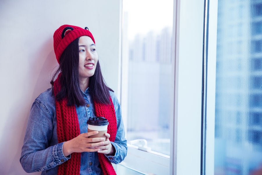 Woman in a red hat drinking coffee and looking out the window.